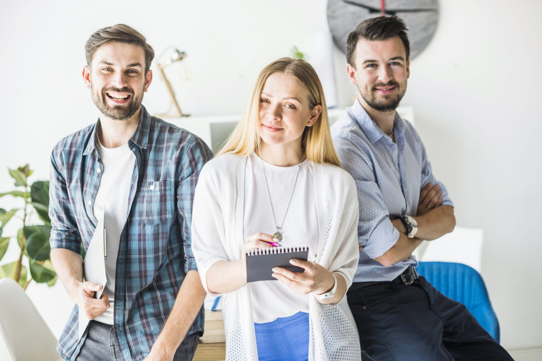 Drei Mitarbeiter lehnen am Schreibtisch und schauen positiv
